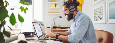 Employee with headphones on sitting at a desk working on a laptop.
