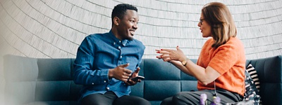 Two employees in conversation with each other while sitting on a couch