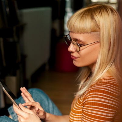 A young student in a library, sitting on the floor, working on an iPad.