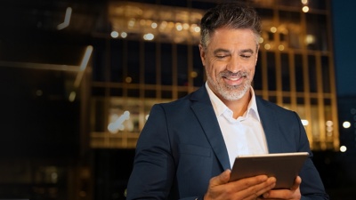 A man stood outside in a city looking at a tablet device