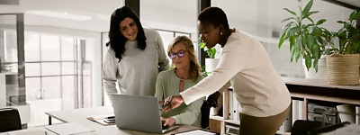 Two coworkers standing up one sitting down on laptop
