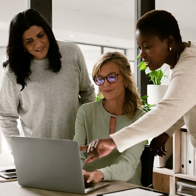 Two coworkers standing up one sitting down on laptop