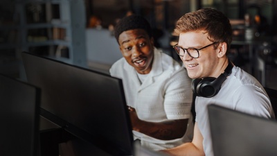 Two colleagues smiling and looking at a computer screen