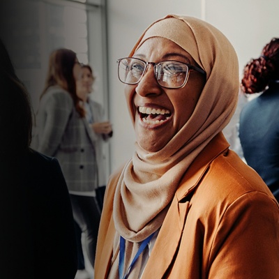 Two women with glasses smile at a conference. 