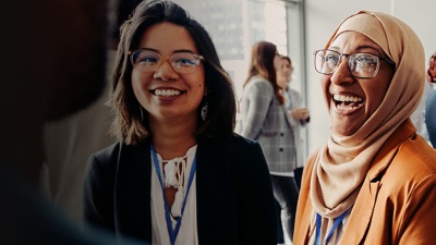 Two women with glasses smile at a conference. 