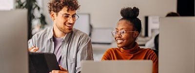 Two people with glasses smiling looking at tablet