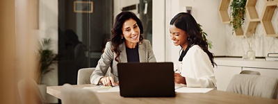 two women sitting at a conference table looking at documents and a laptop