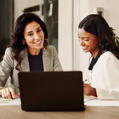 two women sitting at a conference table looking at documents and a laptop