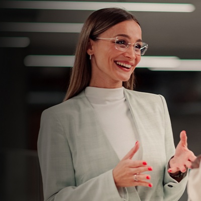 Two women in business attire stand in an office and chat.