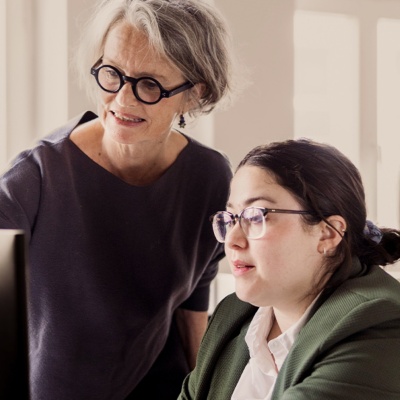 Two women with glasses reviewing work on a computer screen