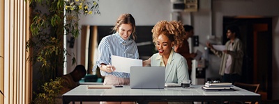 Two women in office smiling looking at laptop