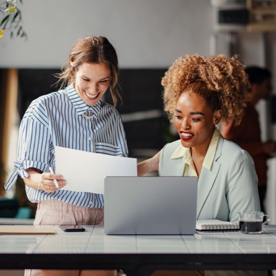 Two women in office smiling looking at laptop