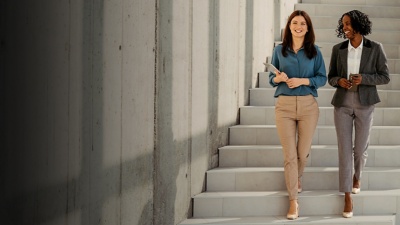 Two female colleagues chat and smile as they descend a staircase. 