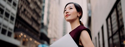 Woman holding laptop looking into the distance.
