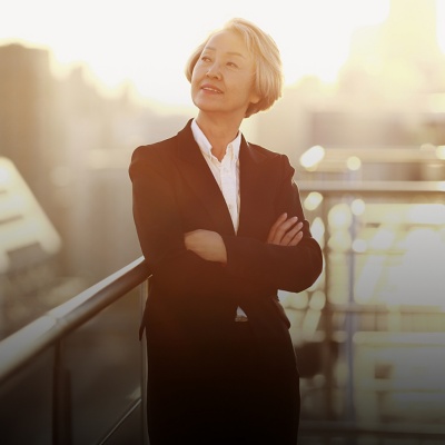 Business person with arms crossed, looking to the side, standing outdoors with office buildings in the background