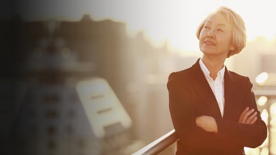 Business person with arms crossed, looking to the side, standing outdoors with office buildings in the background