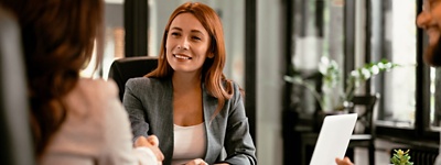 Woman in blazer on laptop shaking hands with client