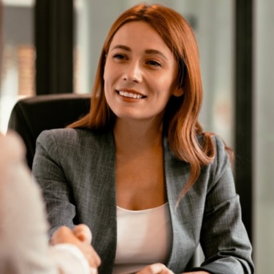 Woman in blazer on laptop shaking hands with client