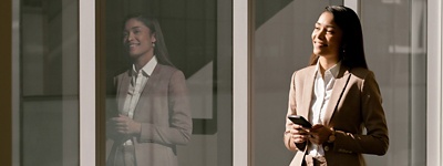 Woman in suit holding phone smiling next to her reflection in the window