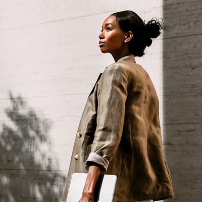 Woman in blazer looking up to the side holding laptop