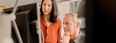 立ったままラップトップを見ている女性と座ったままそれを見ている男性