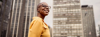 Woman with glasses looking up in front of buildings