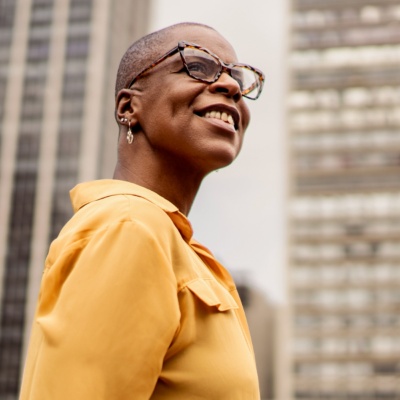 Woman with glasses looking up in front of buildings