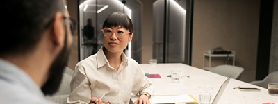 Woman with glasses talking to colleague at table