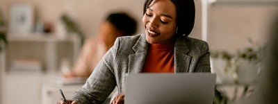 woman-writing-at-desk-in-front-of-laptop